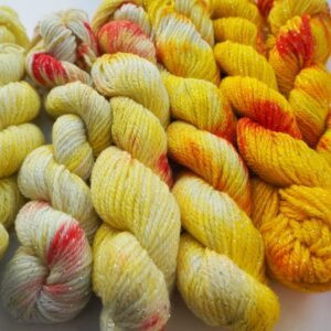 mini skeins of hand dyed yarn in gradient yellow with red speckles on a lurex merino base