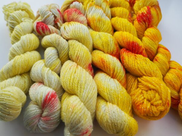 mini skeins of hand dyed yarn in gradient yellow with red speckles on a lurex merino base