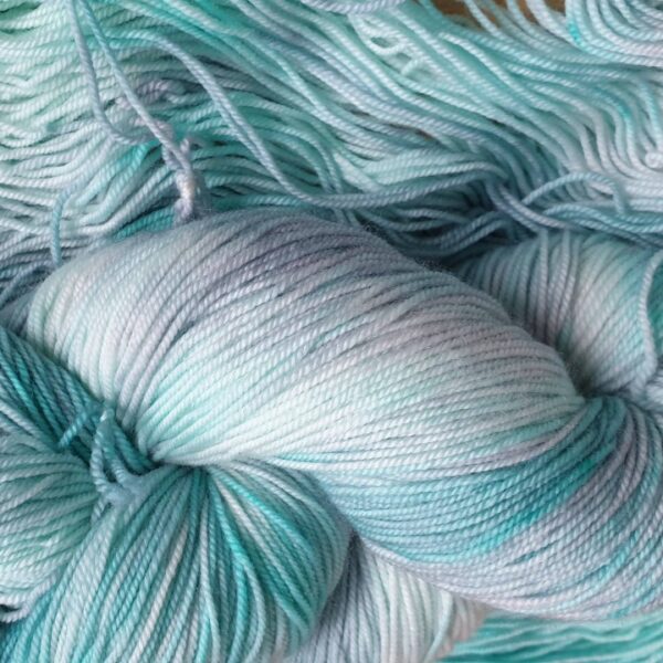 close up of a hand dyed skein of yarn in grey with green streaks