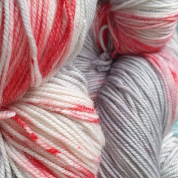 close up of a hand dyed skein of yarn in grey with red stains and speckles