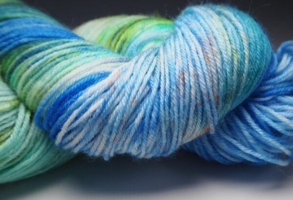 close up of a hand dyed yarn skein in blue and green with yellow and brown speckles