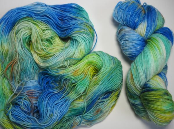 hand dyed yarn skein in blue and green with yellow and brown speckles with the same yarn non wound up on the left